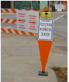 Post-mounted sign located at the point of a sidewalk closure indicates a 'Pedestrian Information Center' with audible information for pedestrians.