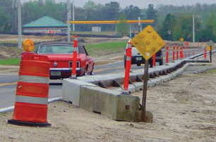 A photo of a construction area to the right of a two-lane roadway in which the travel lane is separated from the work area by low-profile barrier.