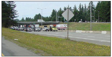 A line of maintenance vehicles with PCMS and Arrow panels, one to each lane, maintains traffic at a slow roll on the approach to a work zone.